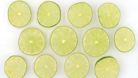Water-splashes-in-slow-motion.-Top-view:-several-lime-circles-washed-by-water-on-a-white-background.-chopped-fruit.